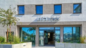 A modern hotel entrance with a glass facade, a clear sky, and a sign reading "NYCE Hotel". - Nyce Hotel Ulm (Ulm)