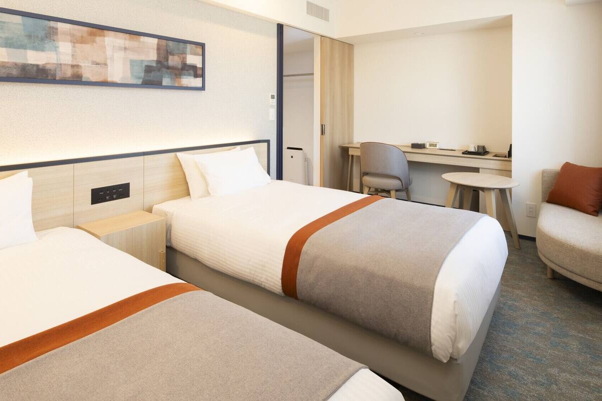 A hotel room with two beds, a desk, a chair, and a sofa.
