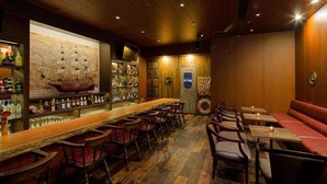 A bar area with wooden flooring, a long bar counter, and multiple seating options including bar stools and tables. - La Gent Stay Shin Sapporo (Sapporo)