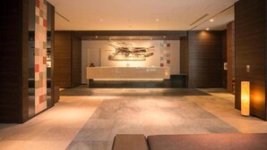A reception area with a modern design, featuring a reception desk, seating area, and a wall-mounted artwork. - La Gent Stay Shin Sapporo (Sapporo)
