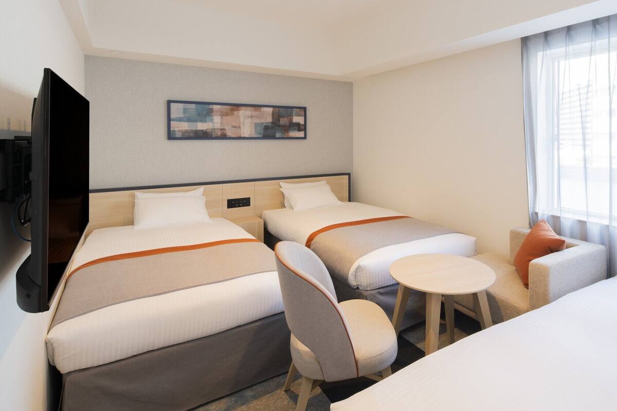 A hotel room with two beds, a TV, a small table, and a window with curtains.