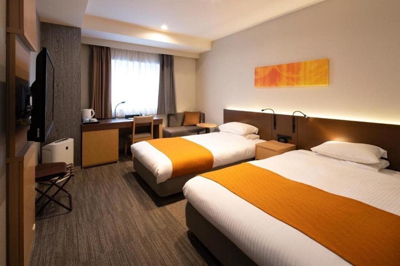 A hotel room with two beds, a desk, a chair, a television, and a painting on the wall.