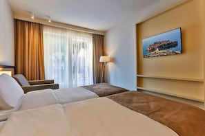 Ett hotellrum med två sängar, ett stort fönster med gardiner, en golvlampa och en tavla som hänger på väggen.