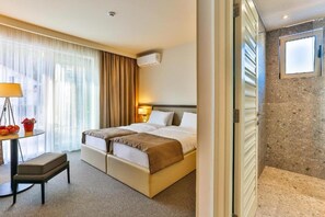 A hotel room with a bed, a desk with a lamp, a chair, and a window with curtains. - Bono Hotel (Bečići)