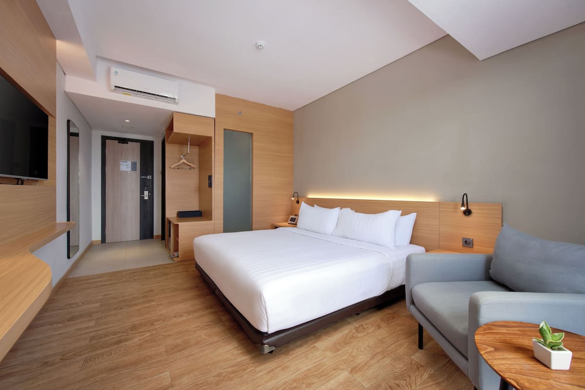 Una habitación de hotel moderna con una cama grande, un sofá, un televisor, una mesita de noche y una planta pequeña.