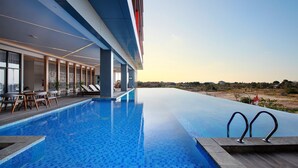 A modern hotel with a large infinity pool, lounge area with chairs, and a view of the landscape. - Harper Kupang (Kupang)
