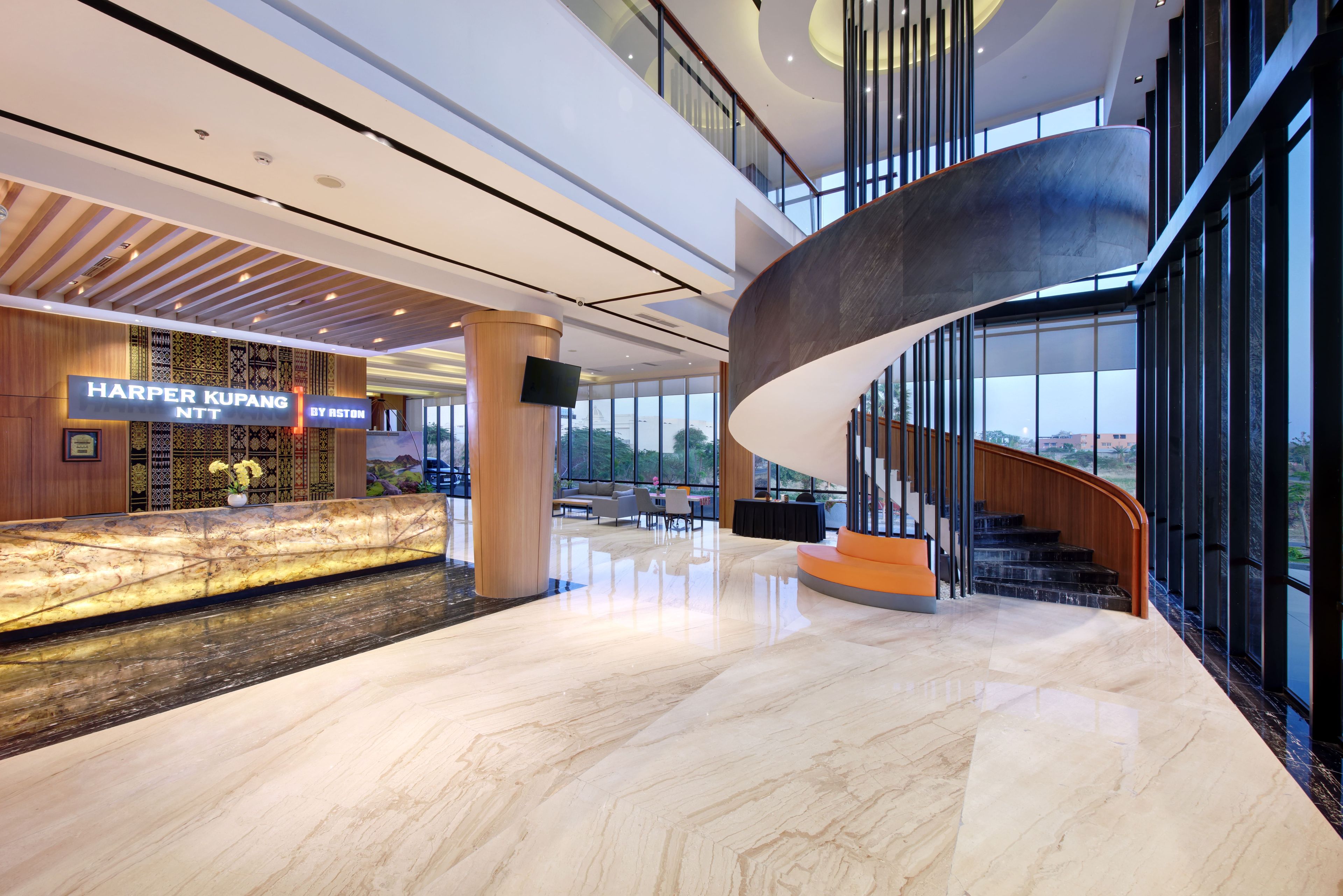 A modern hotel lobby with a marble floor, a curved staircase, and a reception desk with a sign.