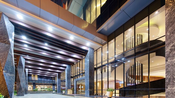 A modern hotel lobby with a spacious entrance, large windows, and a central staircase. - Harper Kupang (Kupang)