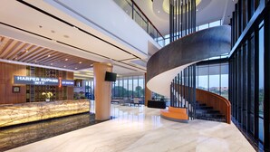 A modern hotel lobby with a marble floor, a curved staircase, and a reception desk with a sign. - Harper Kupang (Kupang)