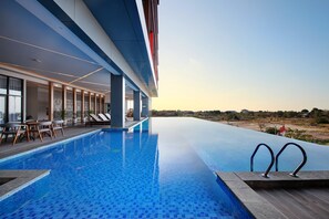 Un hotel moderno con una amplia piscina infinita, un área de descanso con sillas y vistas al paisaje.