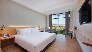 A modern hotel room with a large bed, a desk, a television, and a view of the outdoors.