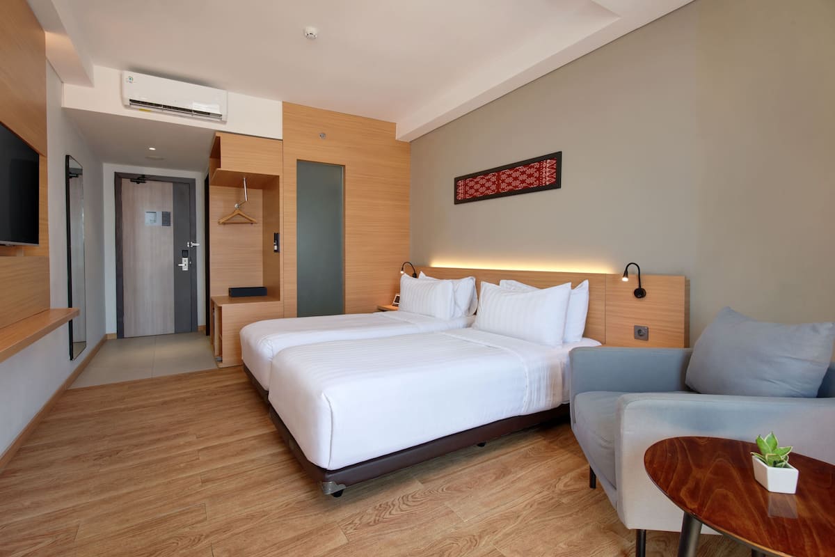 Una habitación de hotel con cama, sofá, una mesita con planta, televisión y aire acondicionado.