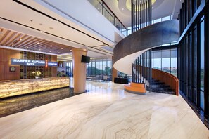 Un moderno vestíbulo de hotel con piso de mármol, una escalera curva y una recepción con un cartel.