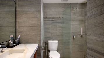Een moderne badkamer met een douchecabine van glas, een wit toilet en een marmeren wastafel.