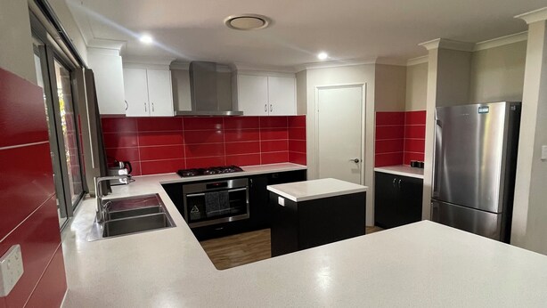 A modern kitchen with white countertops, red backsplash, stainless steel appliances, and a central island. - Rehoboth Landsdale WA (Landsdale)