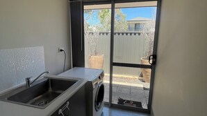 A compact kitchen with a sink, a washing machine, and a sliding glass door leading to an outdoor area. - Rehoboth Landsdale WA (Landsdale)