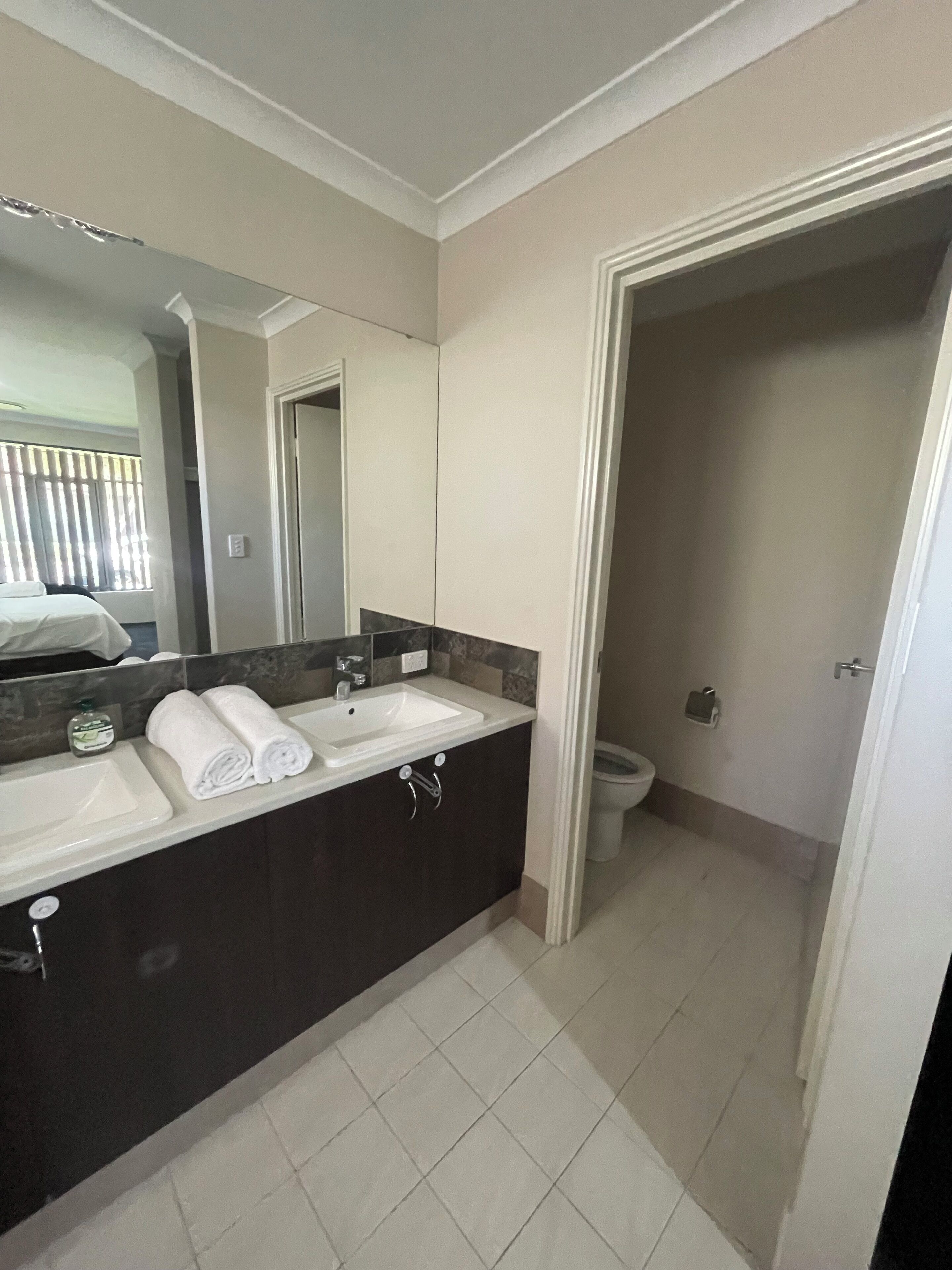 Un baño moderno con un espejo grande, dos lavamanos y un inodoro.