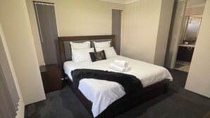 A neatly made bed with white linens and a black throw blanket, a wooden headboard, and a dark carpeted floor. - Rehoboth Landsdale WA (Landsdale)