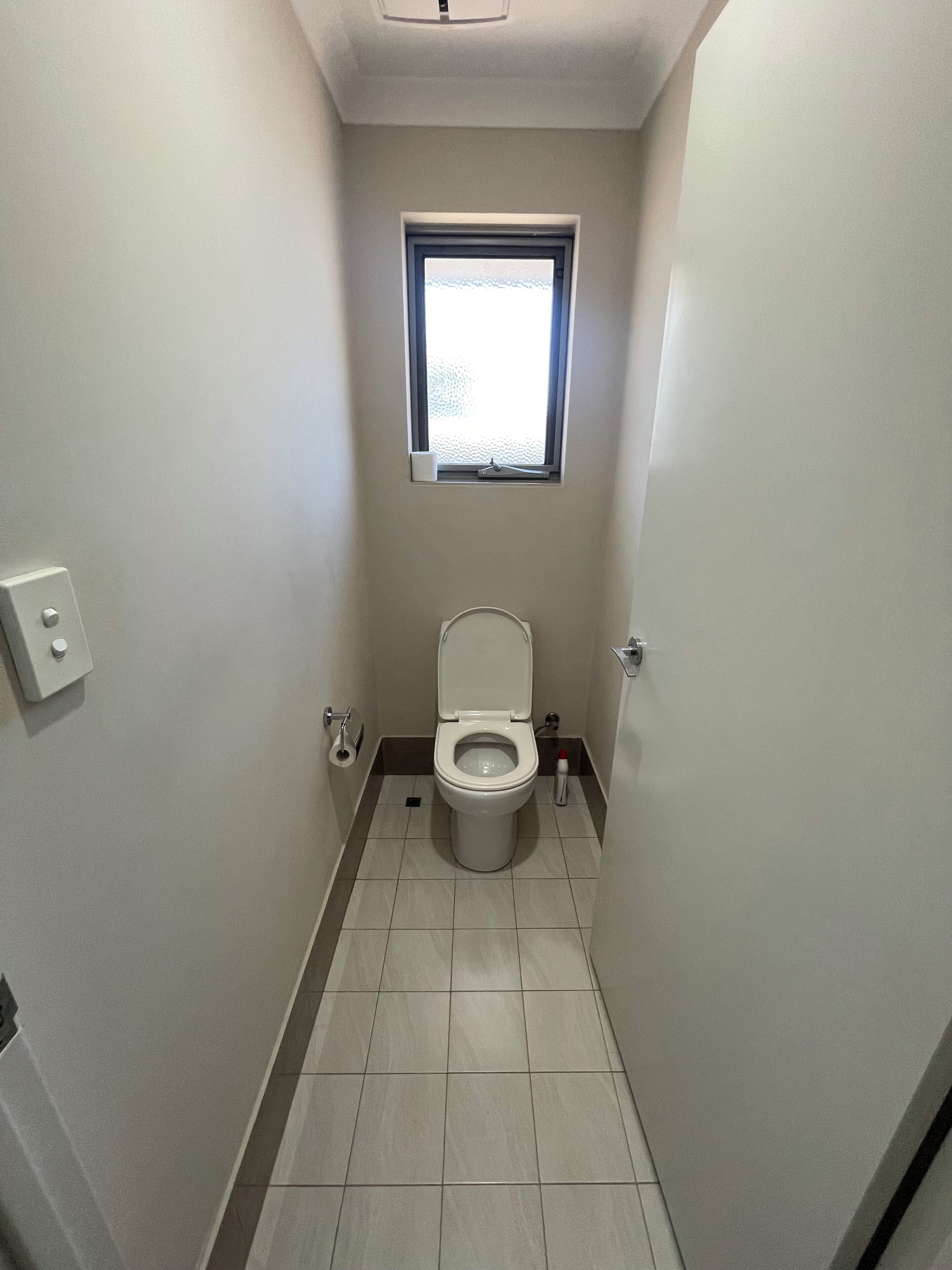 A small, narrow bathroom with a toilet, a window, and a door.