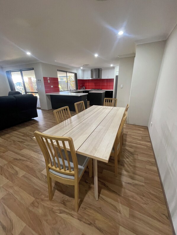 A dining area with a wooden table and chairs, a kitchen with red tiles, and a sliding glass door leading to an outdoor area.