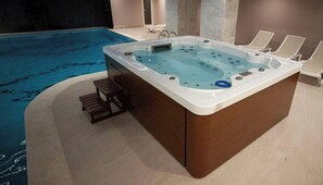 A hot tub with a wooden exterior, adjacent to a swimming pool, and a lounge area with chairs. - Doanesia Premium Hotel and Spa (Kashar)
