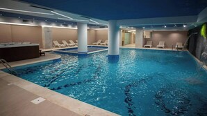 En inomhuspool med klart vatten, solstolar och ett område med bubbelpool.