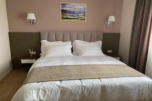 A hotel room with a large bed, two bedside tables, and a painting on the wall. - Doanesia Premium Hotel and Spa (Kashar)