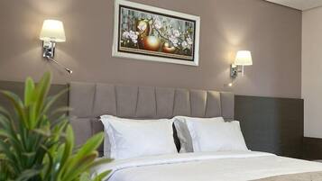 A hotel room with a bed, two wall-mounted lamps, a framed picture above the bed, and a potted plant in the foreground.