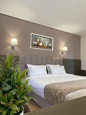 A hotel room with a bed, two wall-mounted lamps, a framed picture above the bed, and a potted plant in the foreground. - Doanesia Premium Hotel and Spa (Kashar)