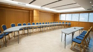 Ett konferensrum med ett långt bord och stolar, stora fönster och en modern takdesign.