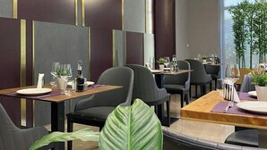 En modern restauranginteriör med högt i tak, hängande lampor och en central sittgrupp omgiven av bord och stolar.