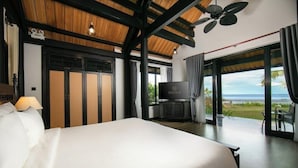 Habitación de hotel con cama, televisor, ventilador de techo y vista al océano.