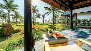 Un espacio de estar techado al aire libre con vistas a palmeras y una piscina.