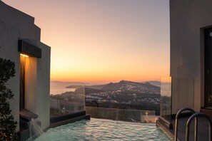 A rooftop infinity pool with a view of a sunset over a coastal city. - Apikia Santorini Suites - Adults Only (Santorini)