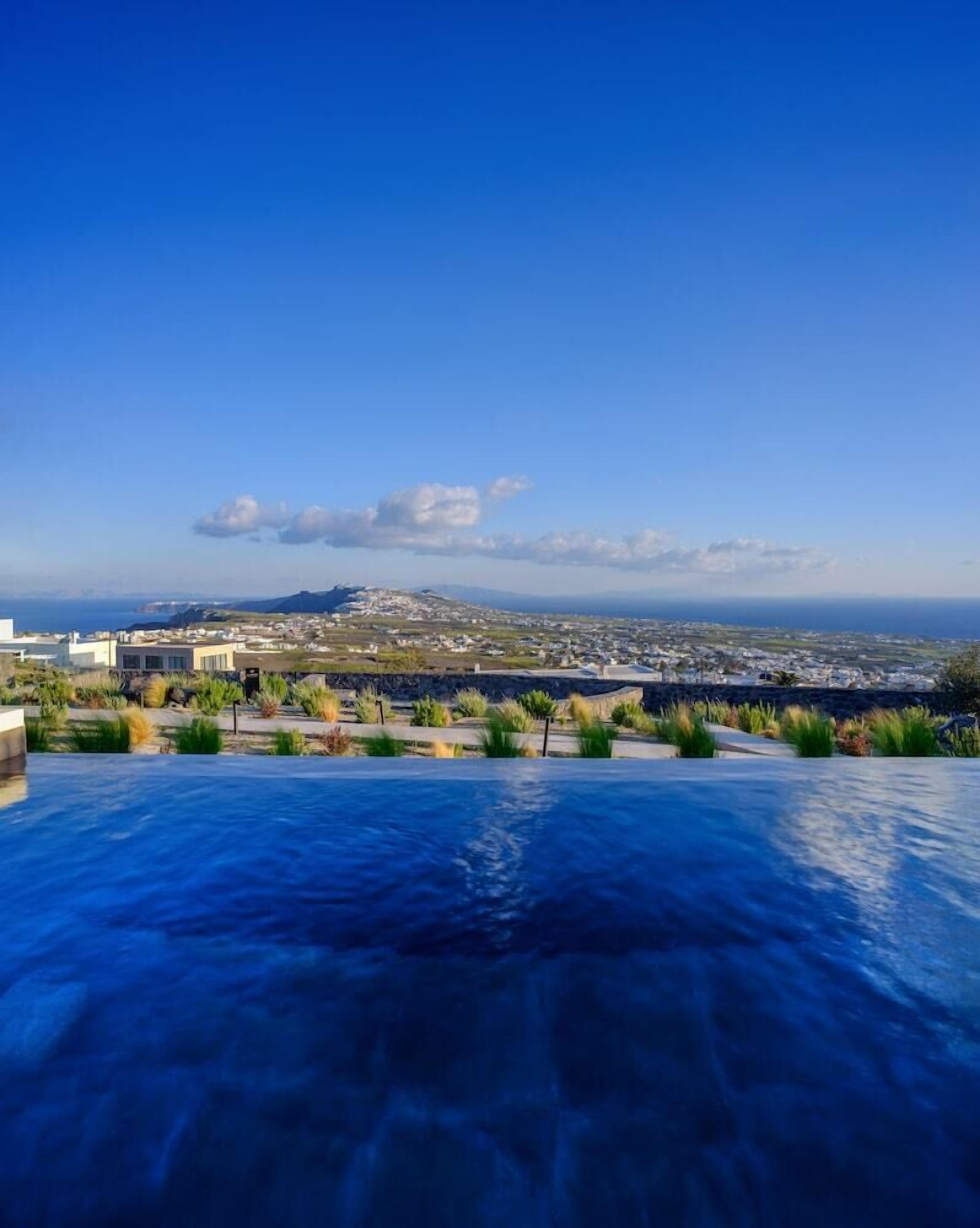 Una piscina infinita en la azotea con vistas despejadas a la ciudad costera y montañas lejanas.