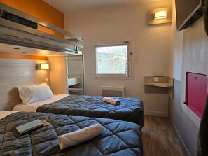 Ein kompaktes Hotelzimmer mit Etagenbetten, einem Fenster mit Blick, einem Nachttisch und einem an der Wand befestigten Fernseher.