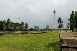 A park with a tall monument, a pond, and a cityscape in the background. - H! Hotel Senen (Jakarta)