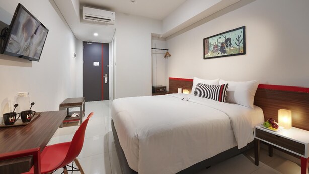 A hotel room with a large bed, a desk with a chair, a TV, and a painting on the wall. - H! Hotel Senen (Jakarta)