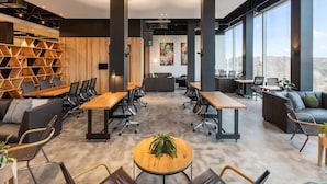 A modern office space with a central meeting table, surrounding seating, and large windows offering a city view. - Sage Ringwood (Melbourne)