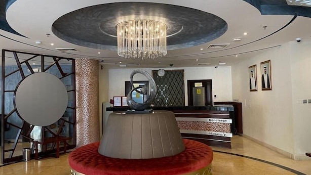 A hotel lobby with a central red cushioned seating area, a chandelier, and a reception desk. - Palm Inn Hotel (Doha)