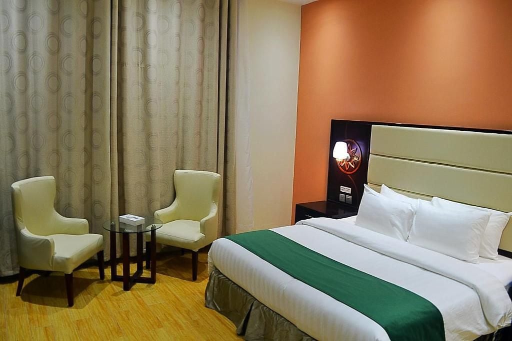 A hotel room with a bed, two armchairs, a small table, and a wall-mounted TV.