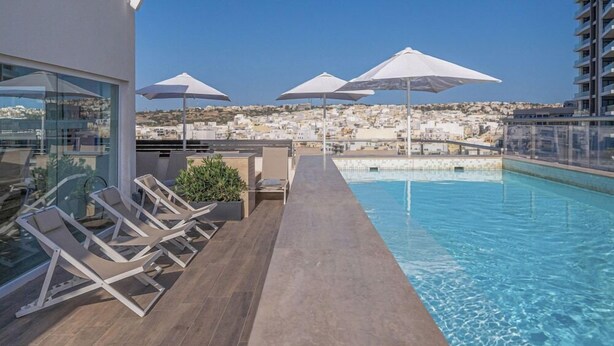A rooftop pool area with lounge chairs and umbrellas, overlooking a coastal town. - Hotel Mistral St. Julian's (St. Julian's)