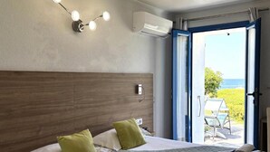 Ein Hotelzimmer mit Bett, Kissen, einem Nachttisch, einer Klimaanlage und Blick durch eine offene Tür.