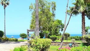 Ein Garten mit Palmen, einer Holzpergola und Blick auf das Meer.