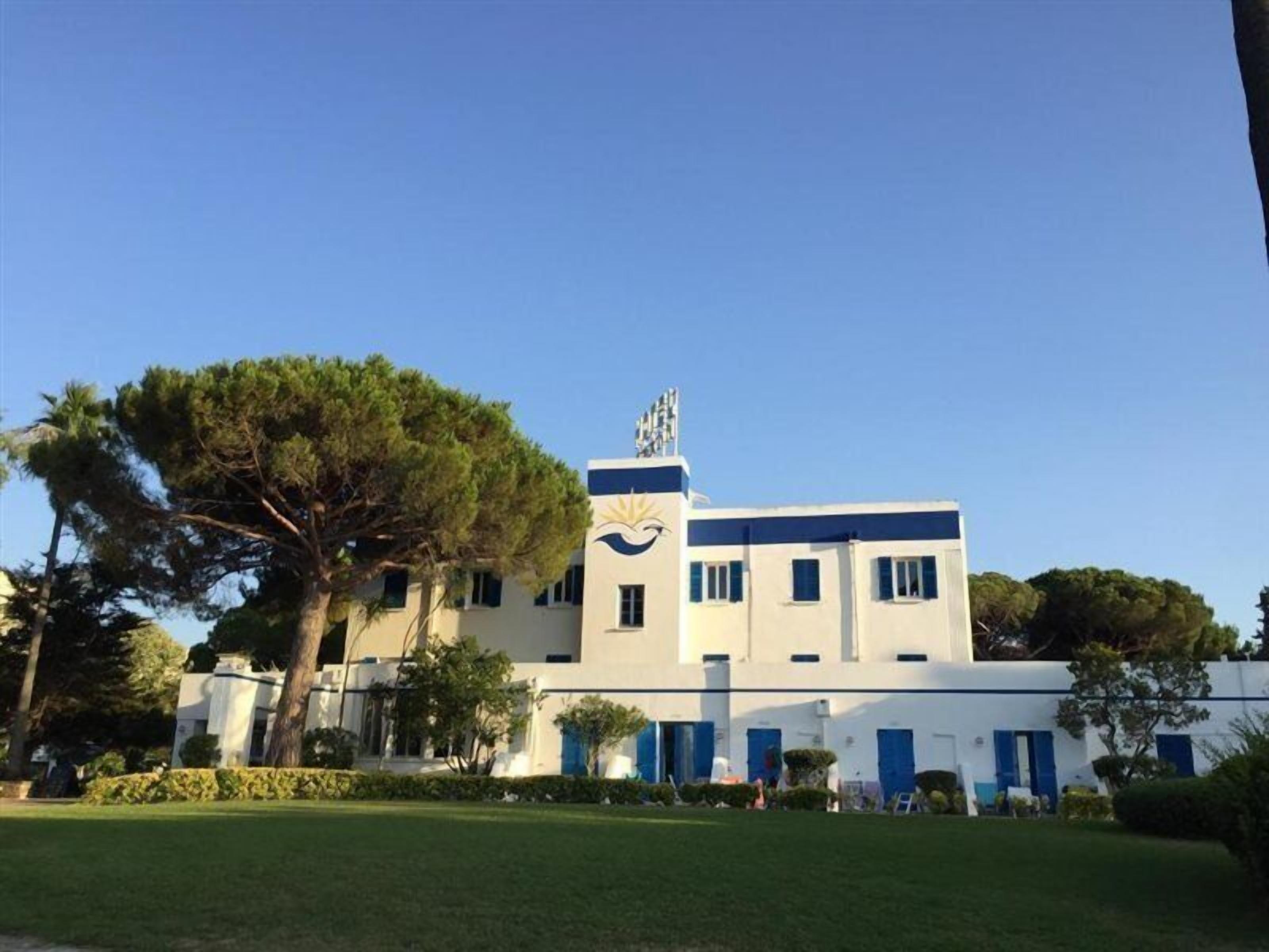 A building with a white facade, blue accents, and a large tree in front.