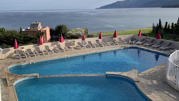 Ein Pool mit Liegestühlen und Sonnenschirmen mit Blick auf ein Gewässer und Berge.