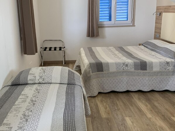 A small, clean room with two beds, a window with blinds, a towel rack, and a wooden floor. - Hotel Bellevue Bastia (Saint-Florent)