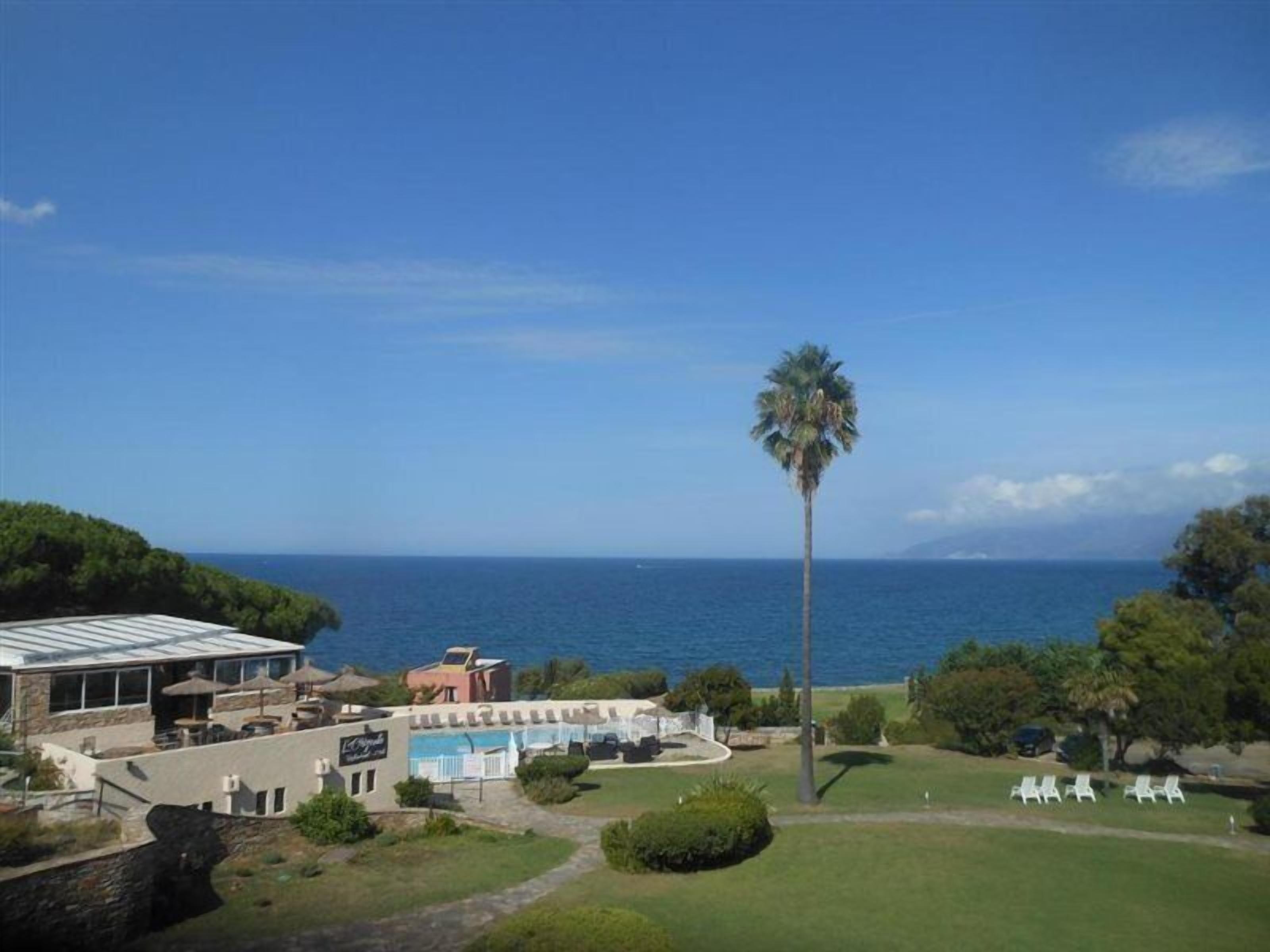 A coastal property with a pool, lounge chairs, and a view of the sea.