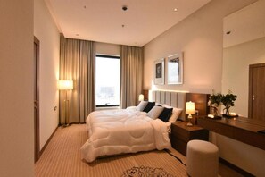 Ein Hotelzimmer mit einem großen Bett, einem Nachttisch mit Lampe, einem Spiegel und einem Fenster mit Vorhängen.