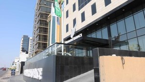 A modern building with a glass facade, a sign reading 'RESIDENCE,' and a flagpole with a flag. - Dream Residence Olaya Khobar (Al Khobar)